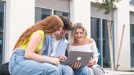 Smiling young friends using laptop outside university buildingの写真素材