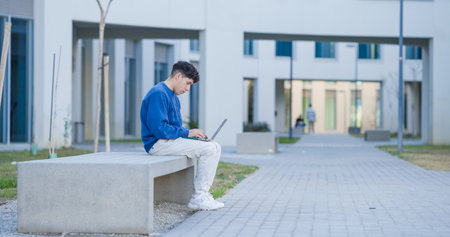 Focused student working on laptop outside university buildingの写真素材