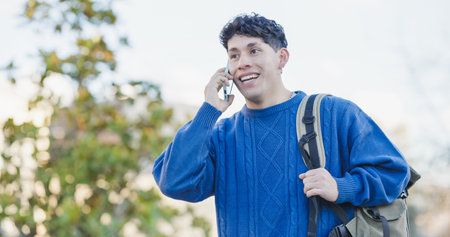 Happy student talking on mobile phone while walking outdoorsの写真素材
