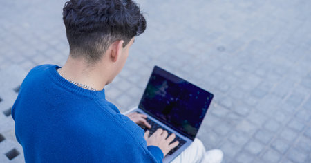 Young student working on laptop outdoors, over the shoulder view