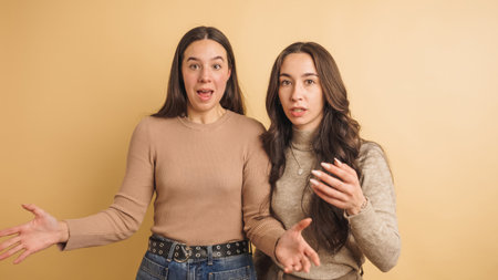 Young women expressing surprise and disbelief against beige backgroundの写真素材