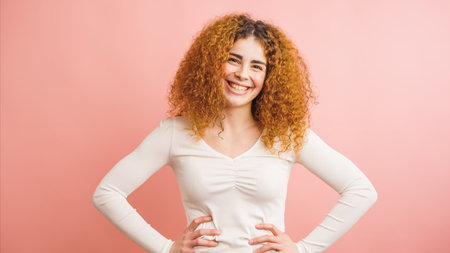 Young woman smiling with hands on hips on pink backgroundの写真素材
