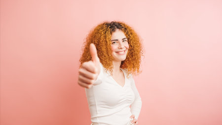 Cheerful woman showing thumbs up sign on pink backgroundの写真素材