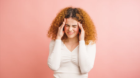 Young woman suffering from strong headache touching temples on pink backgroundの写真素材