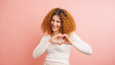 Happy woman showing heart sign with hands on pink backgroundの写真素材