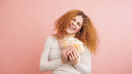 Happy young woman holding euro banknotes and smiling on pink backgroundの写真素材