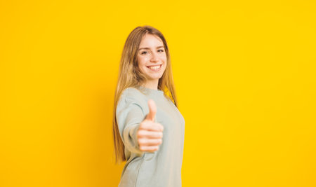 Young woman showing thumbs up sign on yellow backgroundの写真素材