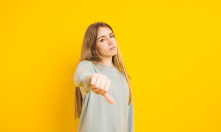 Young woman showing thumbs down gesture on yellow backgroundの写真素材