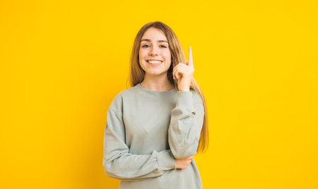 Young woman having an idea pointing upwards on yellow backgroundの写真素材