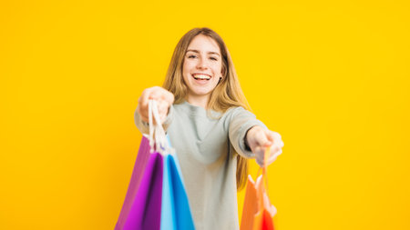 Happy shopper offering colorful shopping bags on yellow backgroundの写真素材
