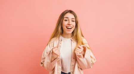 Excited young woman celebrating success on pink backgroundの写真素材