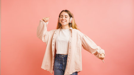 Happy gen z teenager dancing and listening music with headphones on pink backgroundの写真素材