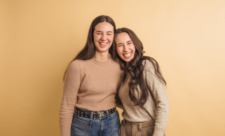 Young female friends laughing together against beige backgroundの写真素材