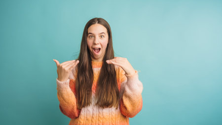 Surprised young woman showing something big with hands on turquoise backgroundの写真素材
