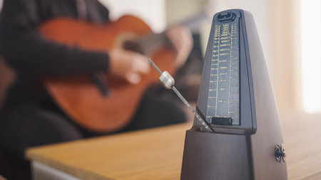 Musician practicing guitar using traditional metronome for rhythmの写真素材