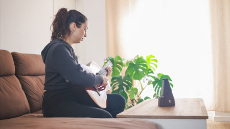 Young woman playing acoustic guitar at home using a metronomeの写真素材