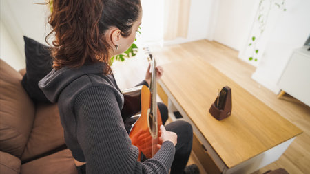 Woman playing acoustic guitar at home with metronome on tableの写真素材
