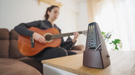 Musician practicing guitar using traditional metronome at homeの写真素材