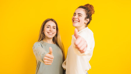Two happy women showing thumbs up on yellow backgroundの写真素材