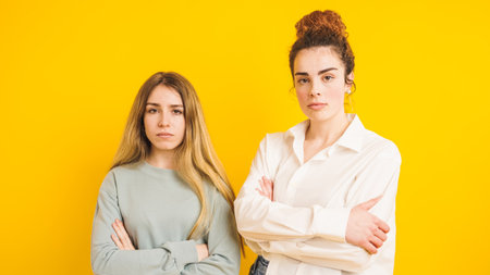 Two serious young women crossing arms on yellow backgroundの写真素材