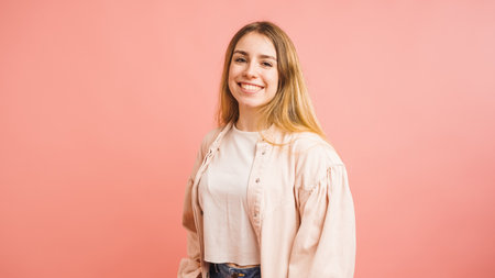 Portrait of smiling young woman with long blonde hair on pink backgroundの写真素材