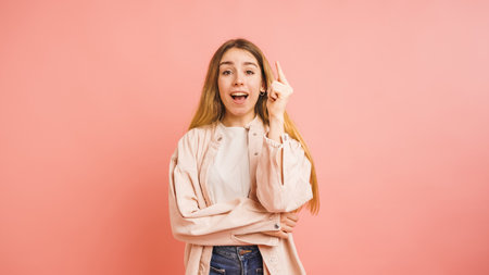 Young woman having an idea pointing upwards on pink backgroundの写真素材