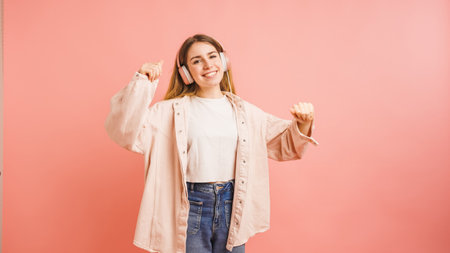 Young woman dancing and listening music with headphones on pink backgroundの写真素材
