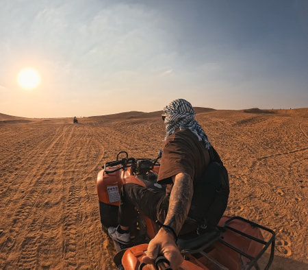 Tourist riding quad bike exploring desert landscape at sunsetの写真素材