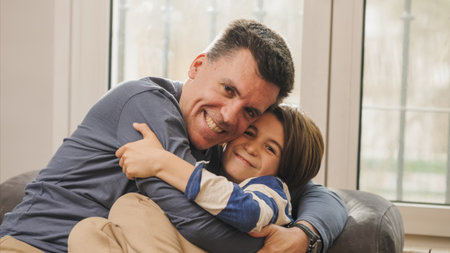 Father and son embracing on sofa, showing love and affectionの写真素材