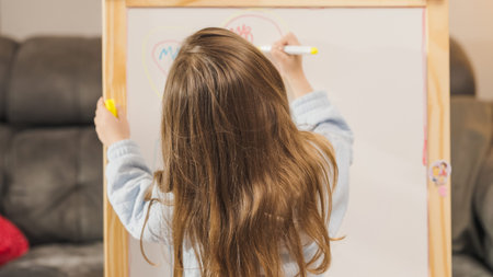 Young girl drawing on whiteboard at homeの写真素材