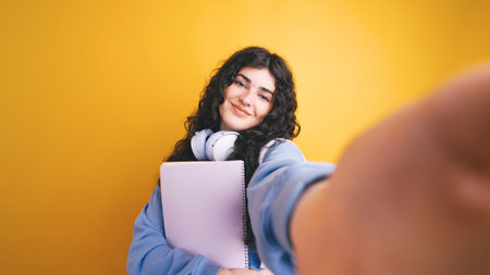 Smiling student taking selfie holding notebook and wearing headphones