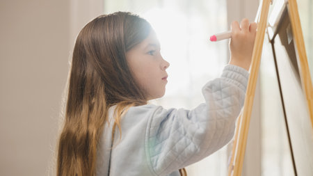 Young girl drawing on whiteboard with pink marker at homeの写真素材
