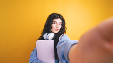 Brunette student taking selfie holding notebook and wearing headphonesの写真素材