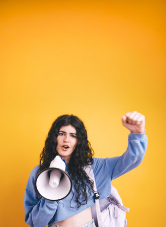 Young student protesting with megaphone on yellow backgroundの写真素材