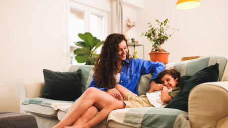 Mother and son tickling and laughing on sofa at homeの写真素材