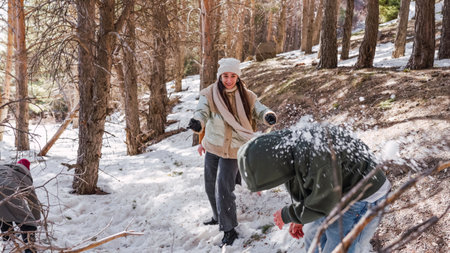 Friends throwing snowballs, enjoying winter fun in snowy forestの写真素材