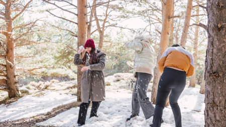 Friends throwing snowballs, enjoying winter fun in snowy forestの写真素材