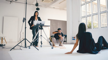 Photographer taking photos of model while art director supervising photoshoot in studio