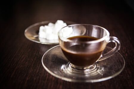 a cup of coffee in front of a blurry plate of sugar cubeの写真素材
