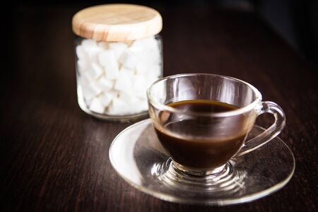 a cup of coffee in front of a blurry  jar of sugar cubeの写真素材