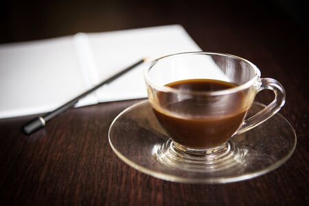 a cup of coffee in front of a blurry pencil and a blurry notebookの写真素材