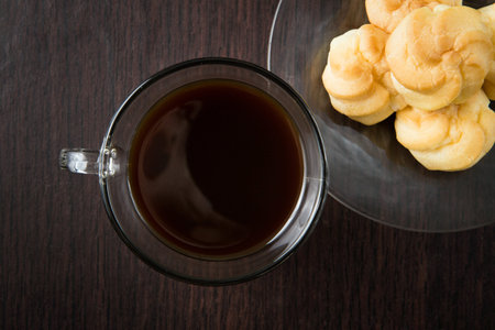 a cup of coffee and a plate of choux cream on the wood table