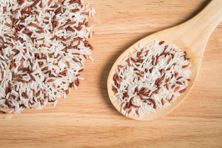 scoop of brown rice and a pile of brown rice on the wood background.の写真素材