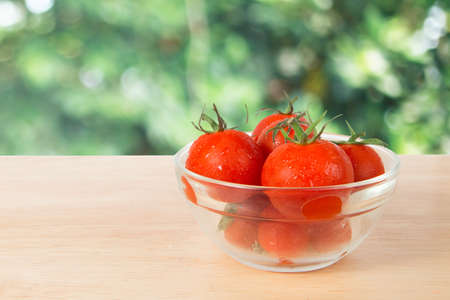 bowl of tomatoes on a wooden block in front of a blurry green  backgroundの写真素材