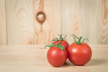 three tomatoes on a wooden block in front of a blurry wooden  backgroundの写真素材