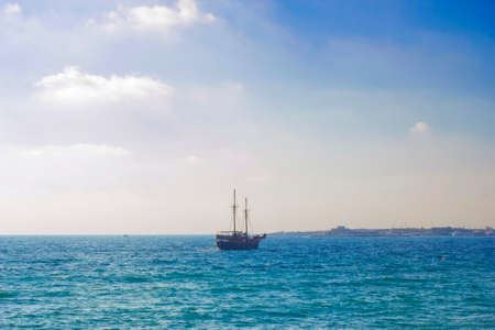 Dark silhouette of ship in sea at sunset, white glare of setting sun on water. Sail boat silhouette at sunset in distance. Sea in eveningの写真素材