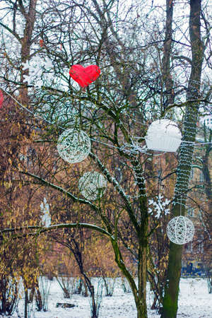 Christmas decorations hanging on tree in park. Hearts, snowflakes and candy decorated tree in winter parkの写真素材