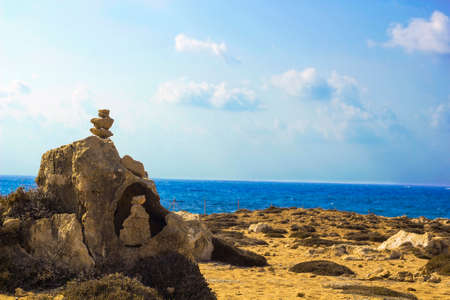Stones pyramid on background of Mediterranean sea. Seashore background with stone tower. Tower of rocks on beach. Small Zen out of pile of stones on rock. Tombs of Kings, an ancient necropolis in Paphos, Cyprusのeditorial素材