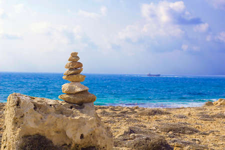 Stones pyramid on background of Mediterranean sea. Seashore background with stone tower. Tower of rocks on beach. Small Zen out of pile of stones on rock. Tombs of Kings, an ancient necropolis in Paphos, Cyprusのeditorial素材