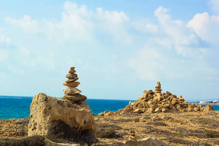 Stones pyramid on background of Mediterranean sea. Seashore background with stone tower. Tower of rocks on beach. Small Zen out of pile of stones on rock. Tombs of Kings, an ancient necropolis in Paphos, Cyprusのeditorial素材